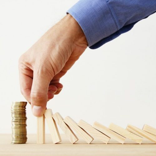 concept image of investing and banking man hands blocking the domino effect, saving a stack of coins